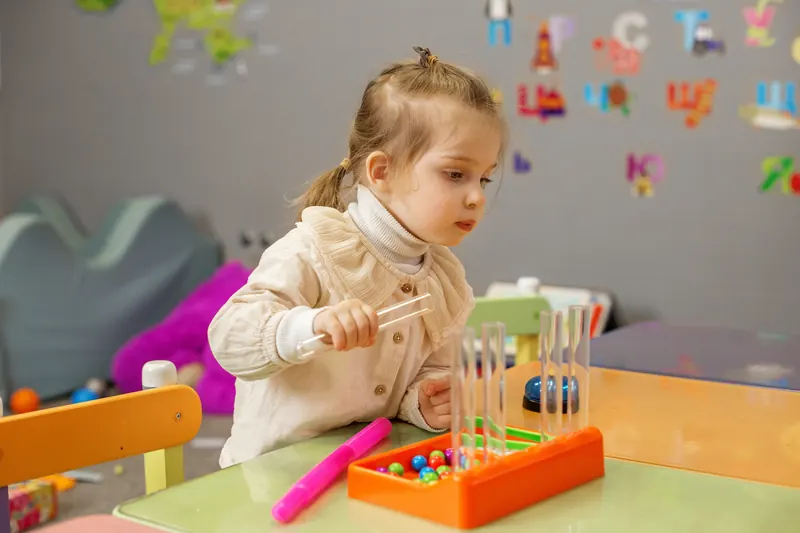 Vorschulkind übt konzentriert Feinmotorik mit Pinzette und Kugeln – spielerische Schulvorbereitung